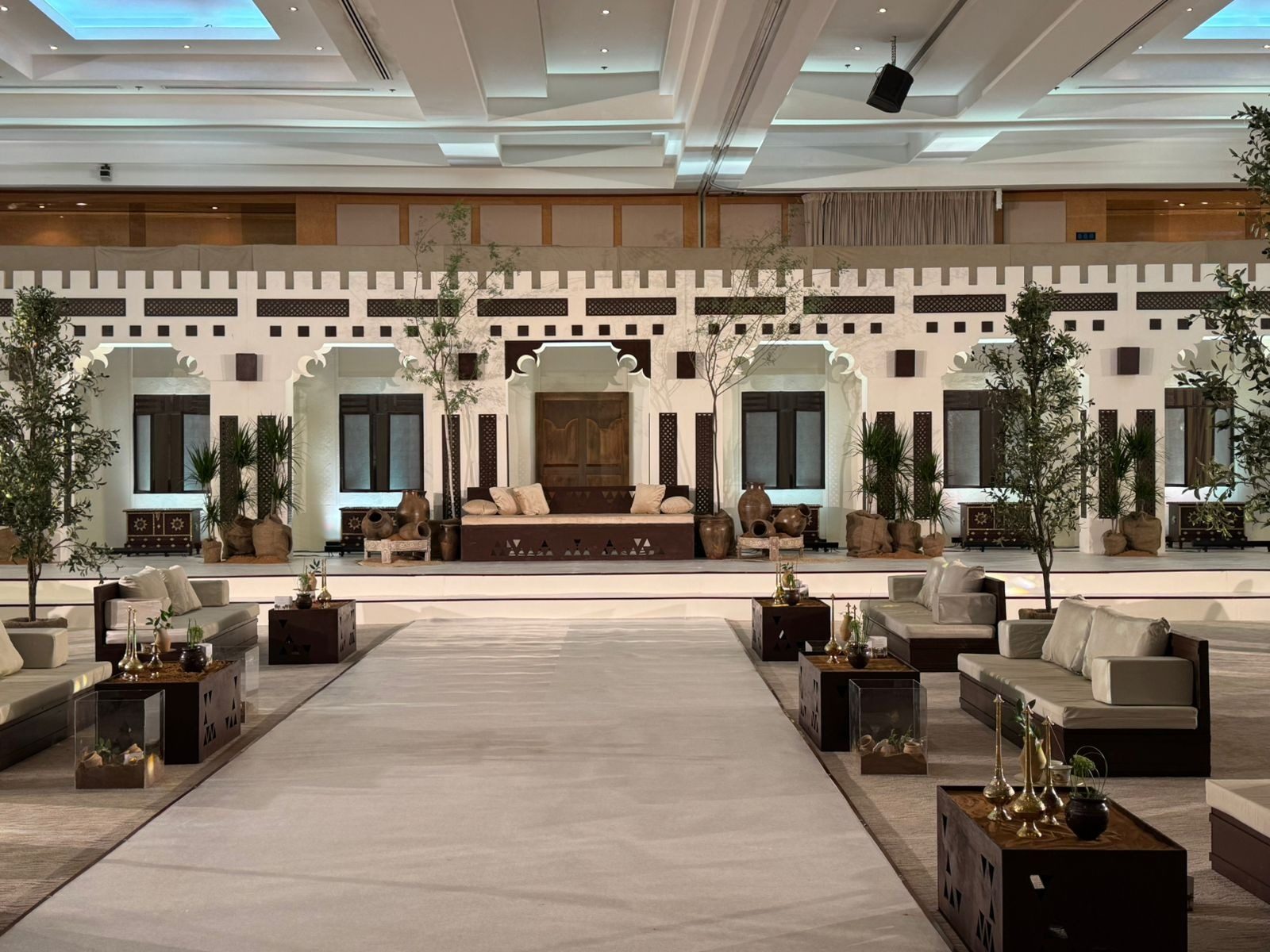 قاعة عرس بتصميم تراثي إماراتي: واجهة حصن بيضاء ونخيل ومجالس على جانبي ممشى العروس